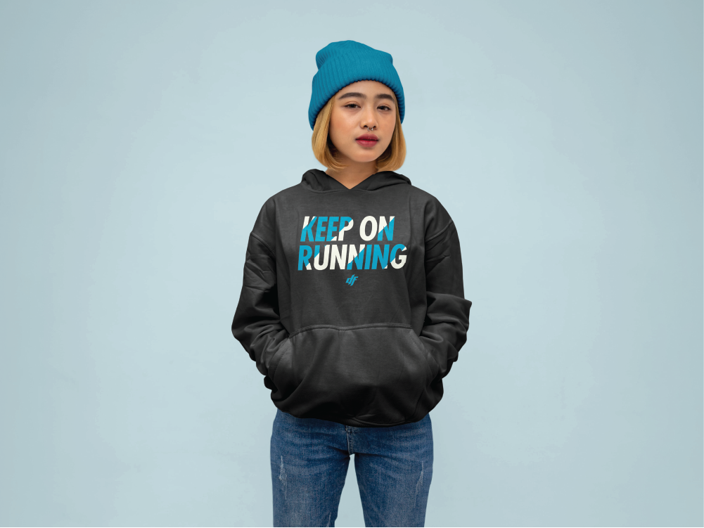 A woman wearing a Diamond Fitness 'Keep on Running' hoodie and a blue beanie, standing confidently against a light blue background, embodying the brand's active and stylish vibe.