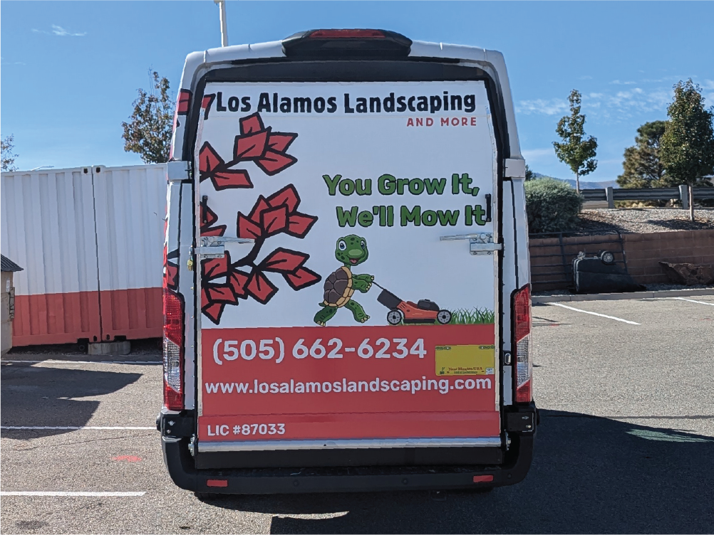 Rear view of Los Alamos Landscaping & More’s Transit van featuring a fun graphic of a turtle pushing a lawnmower with the slogan 'You Grow It, We’ll Mow It!' along with the company phone number and website.