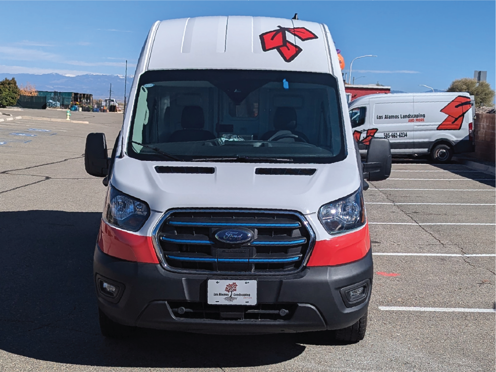 Direct front view of Los Alamos Landscaping & More’s Transit van, displaying the logo on the hood and a strong red accent across the bumper for high visibility.