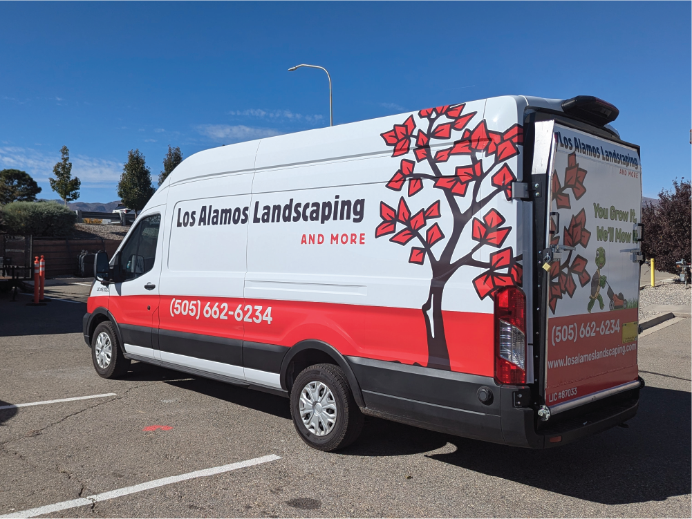 Right side view of Los Alamos Landscaping & More’s Transit van, displaying the company name, phone number, and a large red tree graphic extending from the back toward the front.